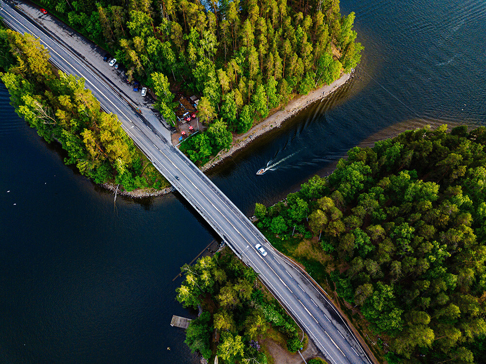 Kesäinen ilmakuva, jossa sillalla auto ja moottoripyörä, vene menee alta.